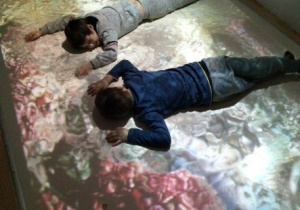 Chłopcy leżą na wizualizacji oceanu na podłodze interaktywnej